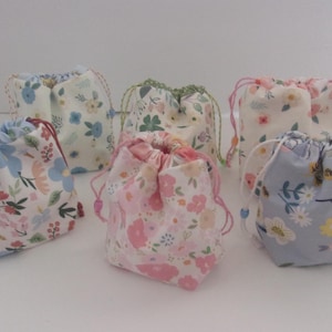 May include: Six small drawstring bags with floral patterns. The bags are made of white fabric with different colored floral prints. The bags are all closed and tied with a drawstring.