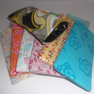 May include: A collection of rectangular fabric pouches featuring various patterns including a black, yellow, and gray swirl design, a turquoise floral print, a pink leaf motif, a bird print, an orange floral pattern, and a yellow fox print.