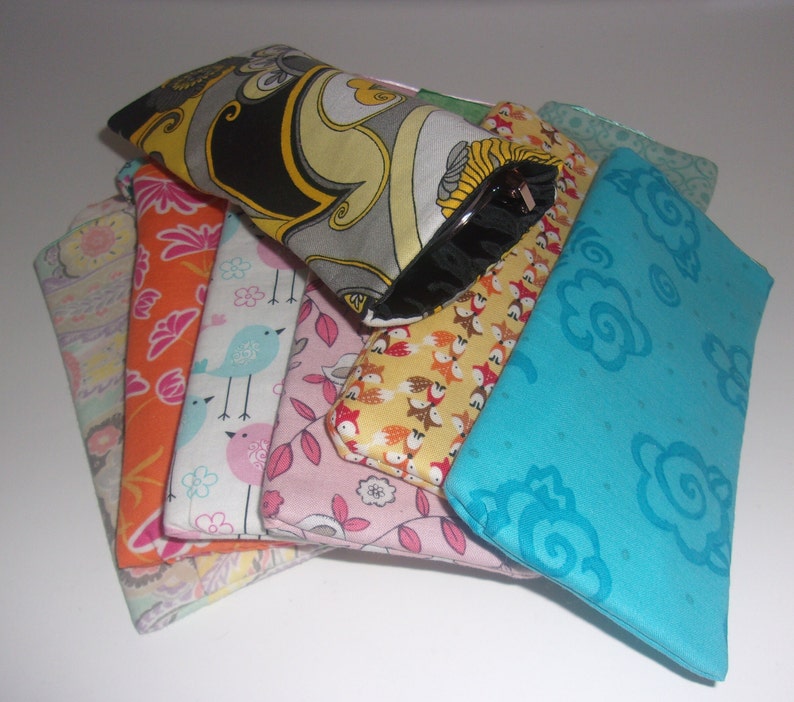May include: A collection of rectangular fabric pouches featuring various patterns including a black, yellow, and gray swirl design, a turquoise floral print, a pink leaf motif, a bird print, an orange floral pattern, and a yellow fox print.