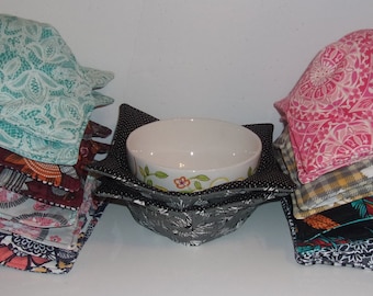 May include: A set of three bowl cozies, each made of different patterned fabric. The cozies are stacked on top of each other. The cozies are in a variety of colors, including teal, pink, black, and white. A white ceramic bowl is sitting on top of a black and white patterned cozy.