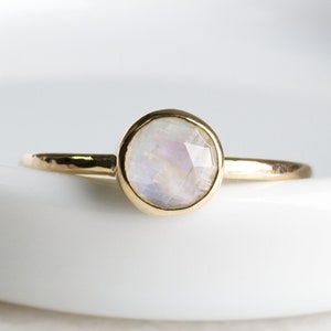 May include: A delicate gold ring with a round, white moonstone gemstone. The ring is simple and elegant, perfect for everyday wear.