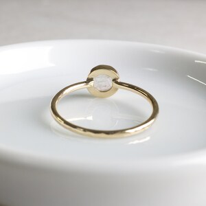 May include: A gold ring with a hammered band and a white oval gemstone.