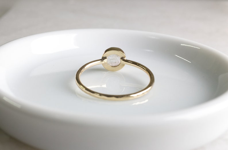May include: A gold ring with a hammered band and a white oval gemstone.