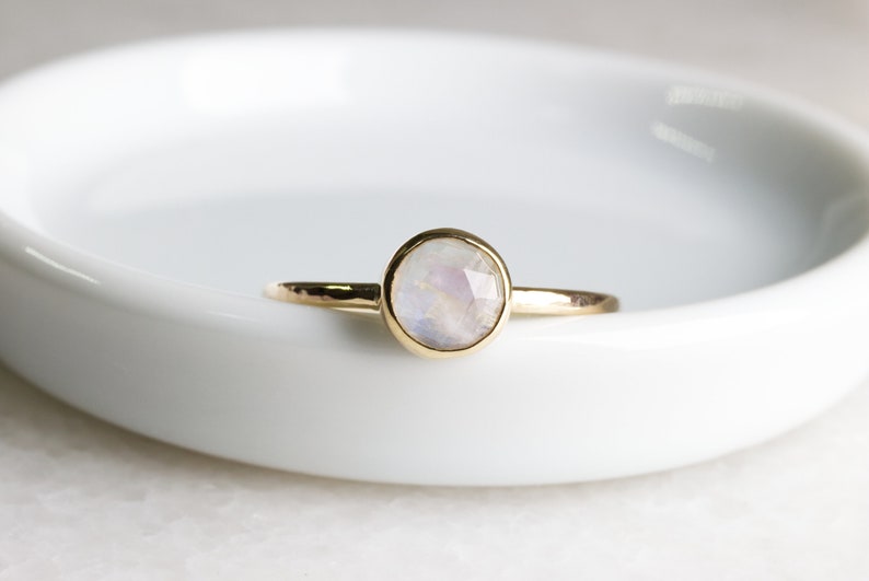 May include: A delicate gold ring with a round, white moonstone gemstone. The ring is simple and elegant, perfect for everyday wear.