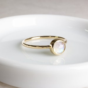 May include: A gold ring with a round, white moonstone gemstone. The ring band is hammered and has a textured finish.
