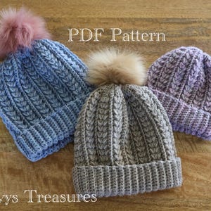 May include: Three crocheted hats with pom poms in shades of blue, grey, and purple. The hats are made with a textured stitch and have a PDF pattern available. The image includes the text "PDF Pattern" and "Ivys Treasures".