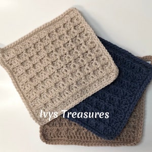 May include: Three crocheted pot holders in beige, brown, and navy blue. The beige pot holder has a waffle stitch pattern. The brown and navy blue pot holders have a braided stitch pattern. The pot holders are stacked on top of each other. The text "Ivys Treasures" is visible on the bottom of the image.