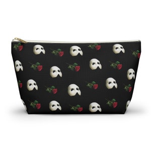 May include: A black zippered makeup bag with a repeating pattern of white Phantom of the Opera masks and red roses.