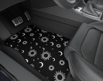 May include: Black car floor mat with a white sun and moon pattern. The mat has a white border and the pattern is repeated throughout the mat.