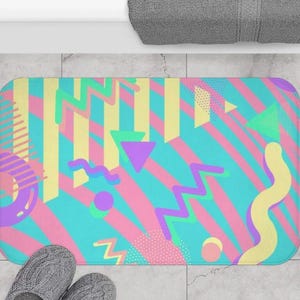 May include: A colorful bath mat with a geometric pattern in shades of pink, blue, yellow, and green. The pattern includes stripes, zigzags, and circles.