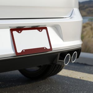 May include: A red license plate frame with a black polka dot pattern is mounted on the back of a white car. The frame has a white interior and is designed to hold a license plate. The car's exhaust pipes are visible.