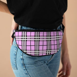 May include: A pink and black plaid fanny pack with a black zipper. The fanny pack is worn around the waist of a person wearing a black shirt and blue jeans.