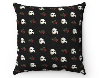 May include: Black and white throw pillow with a repeating pattern of a white Phantom of the Opera mask and a red rose.