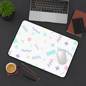 May include: A white desk mat with a geometric pattern in pink, blue, and yellow. The pattern includes circles, triangles, and wavy lines. A white computer mouse is on the mat.