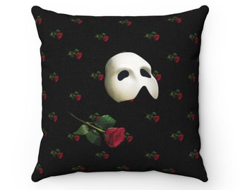 May include: Black throw pillow with a white Phantom of the Opera mask and a red rose with green stem on a black background with a repeating pattern of red roses.