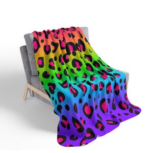 May include: A rainbow colored throw blanket with a leopard print pattern. The blanket is draped over a gray couch.