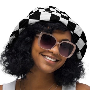 May include: A person wearing a black and white checkered bucket hat with a wide brim and sunglasses. The hat has a simple design with alternating black and white squares.