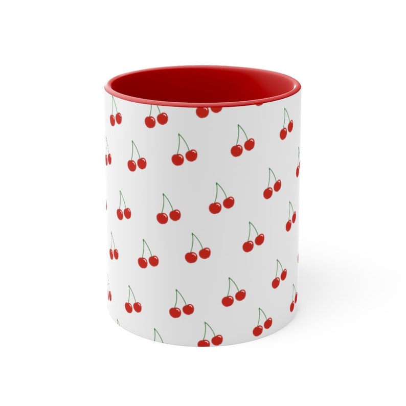 May include: White ceramic mug with a red rim and a repeating pattern of red cherries on a white background.