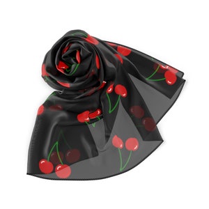 May include: A black sheer scarf with a repeating pattern of red cherries. The scarf is rolled up and tied in a knot.