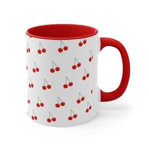 May include: White ceramic mug with a red rim and handle. The mug features a repeating pattern of red cherries on a white background.