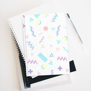 May include: A white notebook with a grid pattern and a colorful geometric design. The design features pink, blue, yellow, and green shapes, including circles, triangles, and wavy lines.