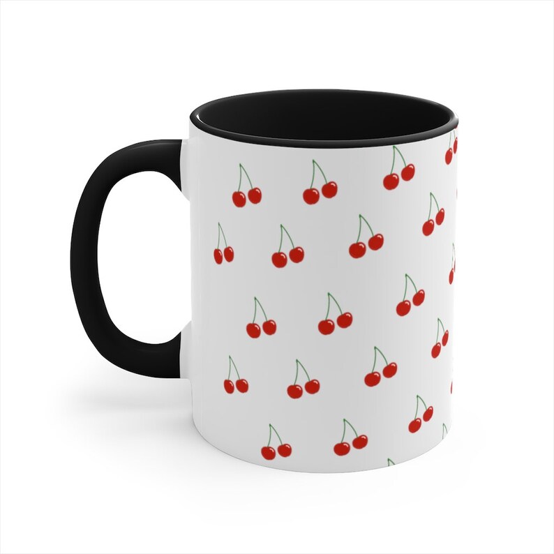 May include: White ceramic mug with a black handle and rim. The mug has a repeating pattern of red cherries on a white background.