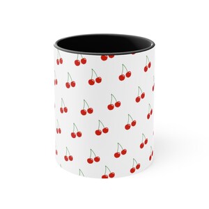 May include: White ceramic mug with a black rim and a repeating pattern of red cherries on a white background.
