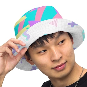May include: A white bucket hat with a geometric pattern in pink, blue, and yellow. The hat has a grid pattern on the underside of the brim.