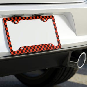 May include: A black and red checkered license plate frame. The frame is made of metal and has a shiny finish.