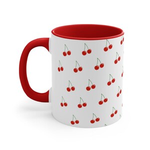 May include: White ceramic mug with a red rim and handle. The mug features a repeating pattern of red cherries on a white background.