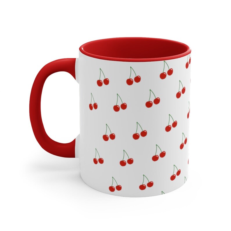 May include: White ceramic mug with a red rim and handle. The mug features a repeating pattern of red cherries on a white background.