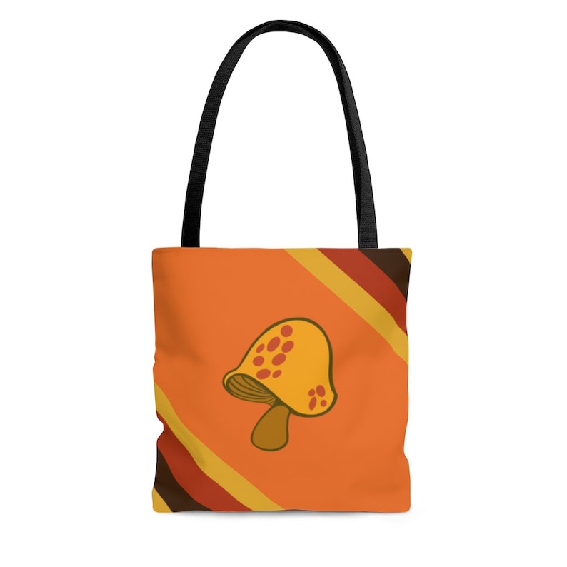 May include: Orange tote bag with a cartoon mushroom graphic. The bag features a yellow mushroom with red spots on an orange background. The design includes diagonal stripes in brown, yellow, and red. It has black handles.