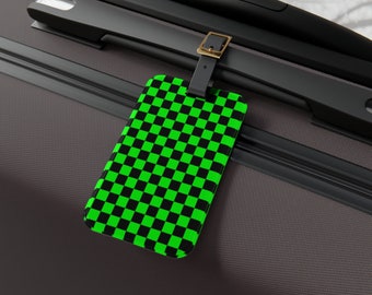 Op de afbeelding: Een zwarte bagagelabel met een groen-zwart geruit patroon. Het label is bevestigd aan een zwarte koffer.