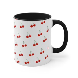May include: White ceramic mug with a black rim and handle. The mug features a repeating pattern of red cherries on a white background.
