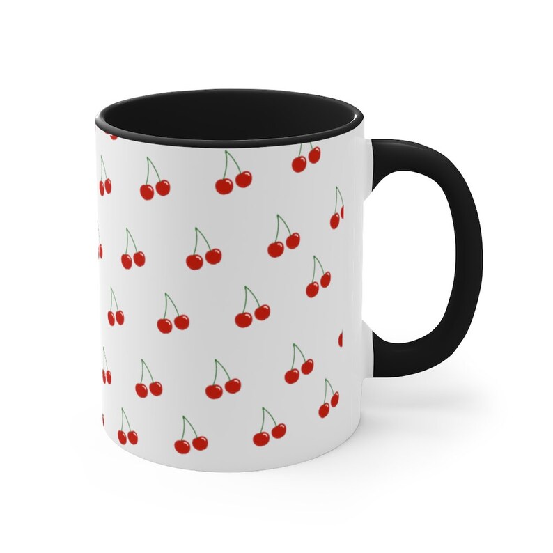 May include: White ceramic mug with a black rim and handle. The mug features a repeating pattern of red cherries on a white background.