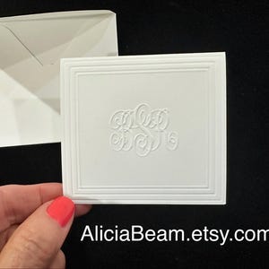 May include: A white rectangular note card featuring an embossed monogram in the center and a decorative border. The card is paired with a matching white envelope. The text AliciaBeam.etsy.com is printed in white at the bottom of the image.