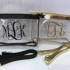 May include: Two clear cosmetic bags with monogrammed initials. One bag has a black trim and black initials, the other has gold trim and gold initials. Both bags have a zipper closure and come with a detachable strap.