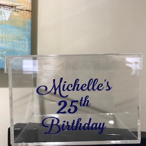 May include: Clear acrylic box with a blue vinyl sticker that says "Michelle's 25th Birthday".