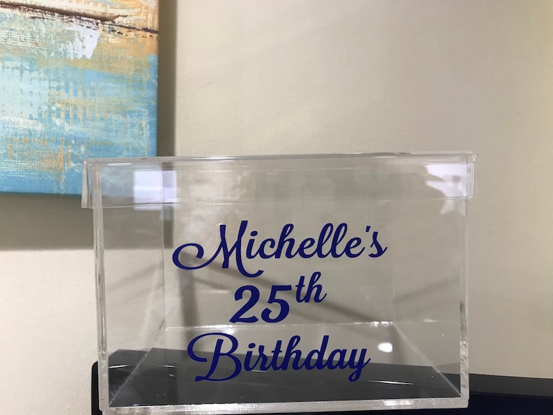 May include: Clear acrylic box with a blue vinyl sticker that says "Michelle's 25th Birthday".