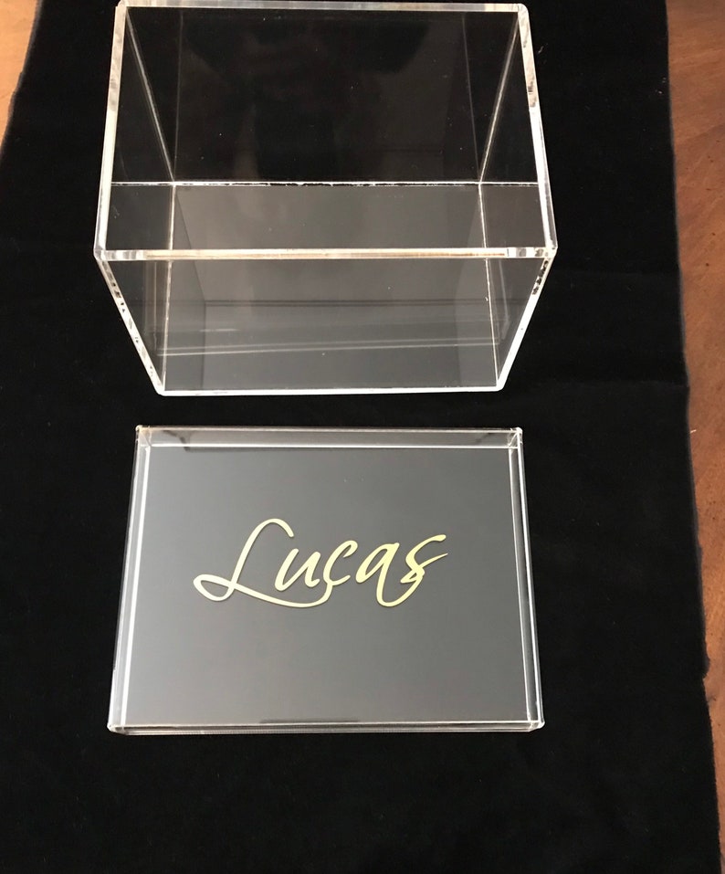 May include: A clear acrylic box with a black lid. The lid has the name "Lucas" written in gold lettering.