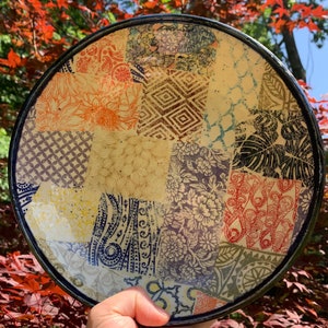 May include: A ceramic plate with a patchwork design featuring various floral and geometric patterns in shades of blue, yellow, red, and brown.