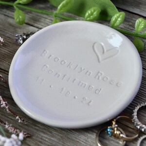 May include: White ceramic ring dish with the inscription "Brooklyn Rose Confirmed 11.18.24" and a hand-drawn heart.