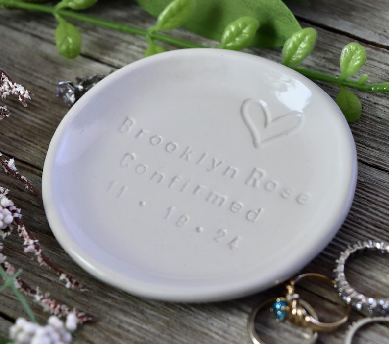 May include: White ceramic ring dish with the inscription "Brooklyn Rose Confirmed 11.18.24" and a hand-drawn heart.