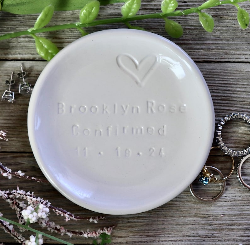 May include: White ceramic trinket dish with a heart design and the text "Brooklyn Rose Confirmed 11.18.24".