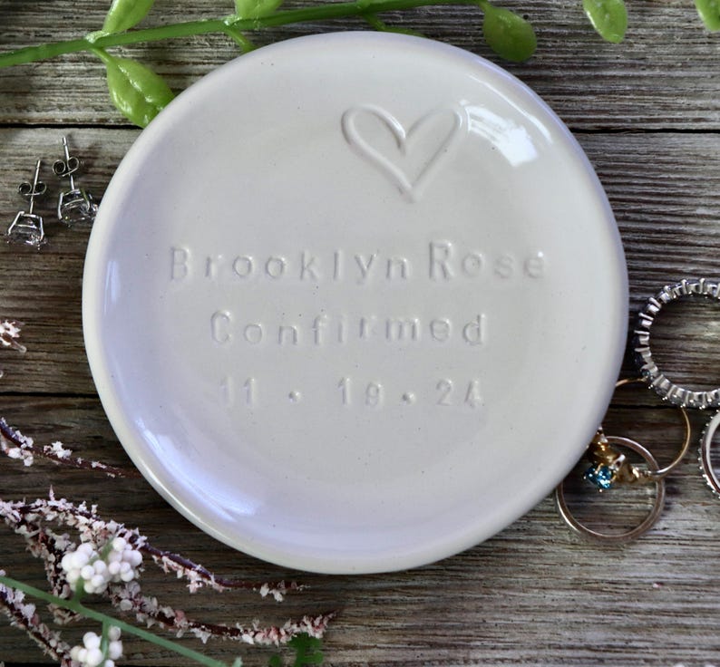 May include: White ceramic trinket dish with a heart design and the inscription "Brooklyn Rose Confirmed 11.18.24".