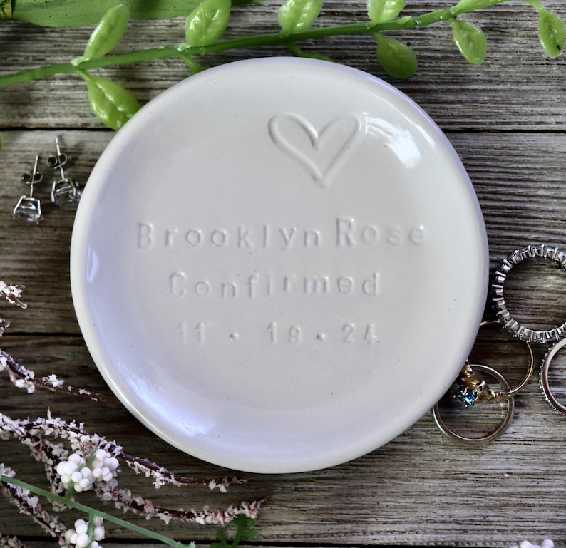 May include: White ceramic ring dish with a heart design and the text "Brooklyn Rose Confirmed 11.18.24".