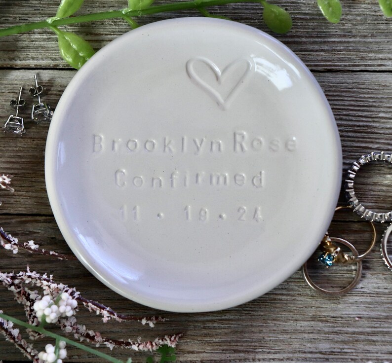 May include: White ceramic ring dish with a heart design and the inscription "Brooklyn Rose Confirmed 11.18.24".