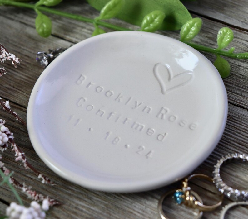 May include: White ceramic ring dish with the inscription "Brooklyn Rose Confirmed 11.18.24" and a hand-drawn heart.