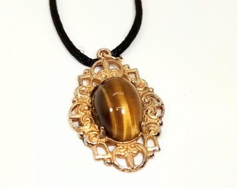 May include: A gold-colored pendant necklace with a tiger's eye stone. The oval-shaped stone is set in a decorative, filigree-style frame. The necklace has a black cord.
