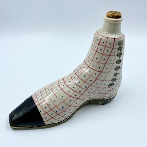 May include: A ceramic bottle shaped like a shoe with a checkered and polka dot pattern in pink and blue. The bottle has a cork stopper and a black toe.